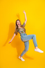 Naklejka premium Young woman jumping in bright yellow studio wearing floral top jeans and sneakers enjoying fashion lifestyle