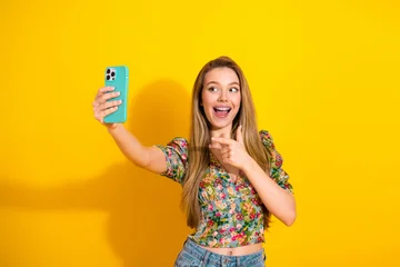 Fotobehang Lieveheersbeestjes Young woman takes a cheerful selfie against a vibrant yellow background in a floral top  © deagreez