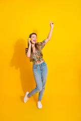 Fotobehang Cars Young woman dancing with headphones against bright yellow background wearing floral top and jeans for lifestyle fashion and music vibe  © deagreez