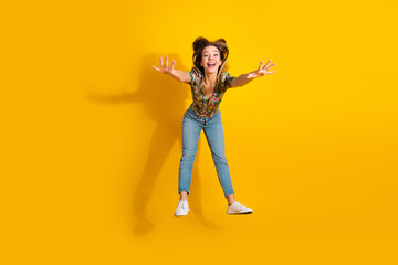Joyful young woman jumps in a bright yellow studio showcasing fashion style and playful lifestyle