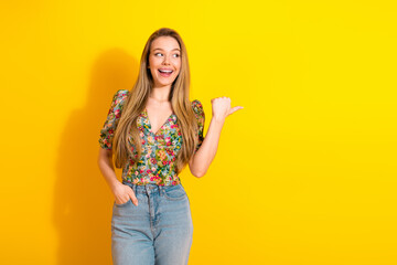 Young chic woman in floral top and jeans smiles against a bright yellow background