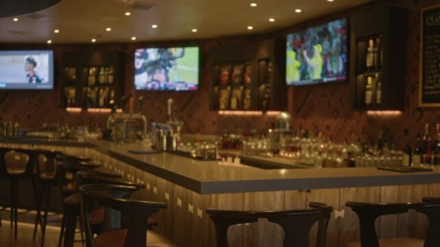 Blurry sports bar scene with shallow bokeh and out of focus tv screens and stools under warm ambient lighting interior; copyspace backplate overlay calm.