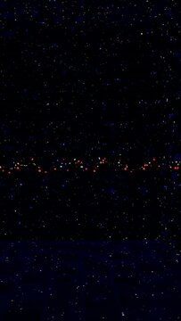 Vertical video: Filming string of colored lights twinkling at night over dark horizon, starry sky