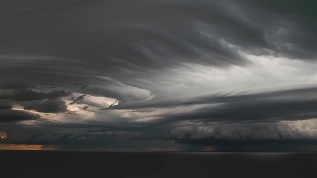 Heavy, layered storm clouds dominate the sky above a dark ocean, with streaks of sun breaking through, symbolizing impending change and nature's raw power.