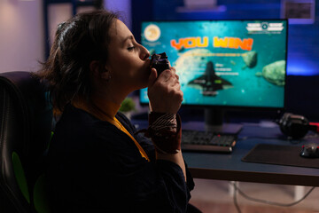 Cheerful adult kissing controller after winning video games. Woman feeling happy about win, using joystick on computer to play online game. Gamer with technology playing on internet. © DC Studio