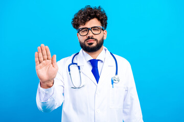 Male doctor in white coat and stethoscope making stop gesture with hand expressing refusal or...