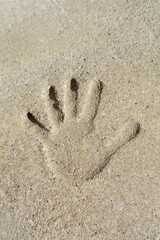 A top down view showing a deep impression of a human hand with spread fingers pressed into a rough grainy beige concrete surface