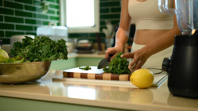 Healthy lifestyle scene with Close-up of an Asian woman slicing fresh kale in a kitchen while preparing ingredients for a green smoothie