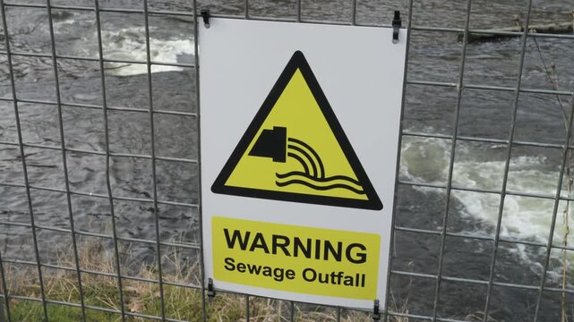 Sewage Pipe outfall warning sign on a fence with flowing river