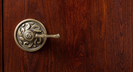 Fototapeta premium Decorative brass door handle featuring elegant swirling curves on deep brown wood with copy space
