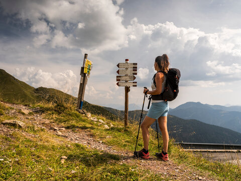 A hiker with a backpack and poles stands at a trail signpost, overlooking mountains. Monte Crostis,Carnia,Friuli Venezia Giulia,Italy