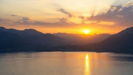 Obraz premium Lake surface mirroring sunrise over distant mountain range.