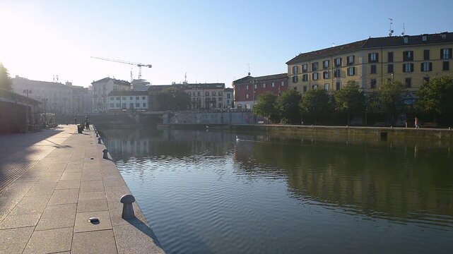 Morning sunlight over Darsena waterfront in Milan, Navigli district, canal with swan swimming, urban promenade and historic buildings in Lombardy, Italy