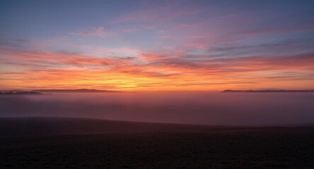 Obraz premium Dusk scene of a foggy landscape with vibrant sunset and fading light