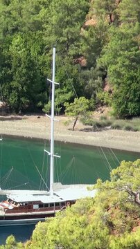 Traditional Turkish gulet floats peacefully in clear turquoise waters of Aegean Sea cove near Oludeniz, Fethiye. Lush green forests flank sandy shore, overlooked by Babadag Mountain. Perfect day.