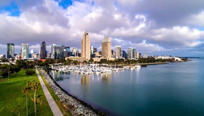 Fototapeta premium A scenic panoramic vista of a modern city skyline. A body of water with moored boats in front. Cloudy skies