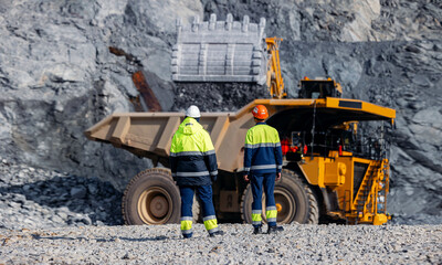 Work team engineers supervise loading of gold ore by excavator into large quarry yellow truck. Concept open pit mine industry.