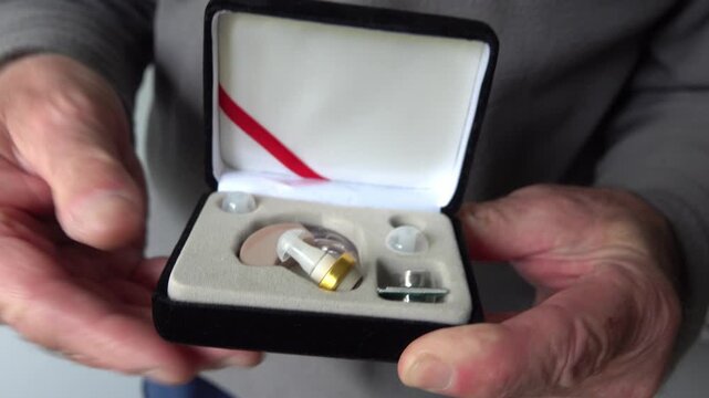 Person holds open case with hearing aid and shows device