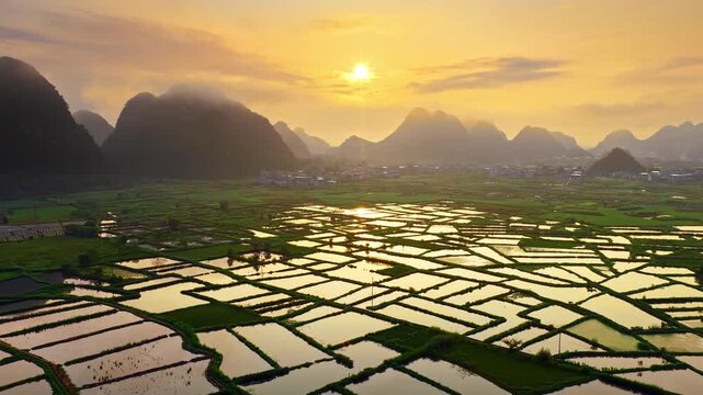 Scenic aerial view of limestone karst mountains and flooded rice paddies reflecting golden sunset light in Guilin, China.
