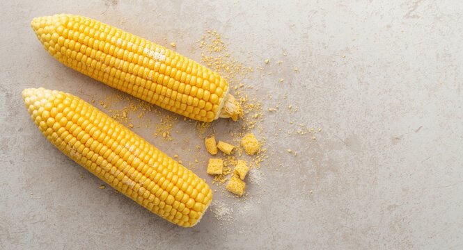 Bright yellow corn ears on rough tabletop with cornstarch sprinkled nearby