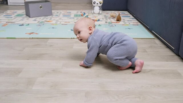 Adorable six-month-old baby boy wearing a grey romper learning to crawl on the wooden floor of his playroom, exploring his surroundings during a significant developmental milestone