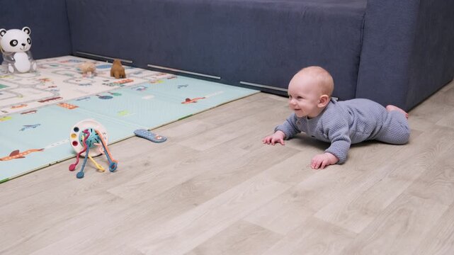 Curious little baby boy learning to crawl for the first time on the wooden floor at home. Adorable infant exploring the room, developing motor skills, and achieving a new milestone