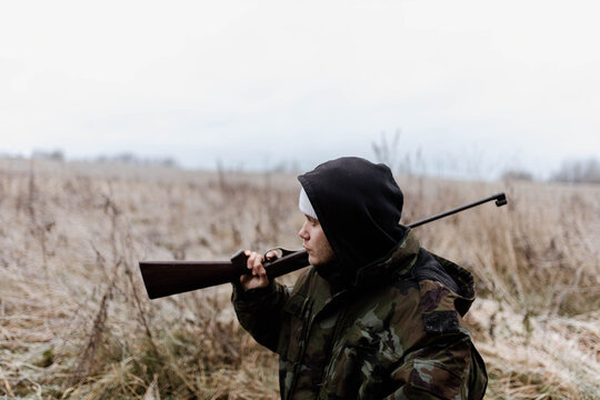A male hunter with a gun in a camouflage jacket in a field in cold weather