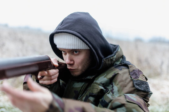 A male hunter with a gun in a camouflage jacket in a field in cold weather