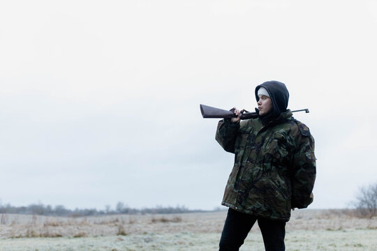 A male hunter with a gun in a camouflage jacket in a field in cold weather