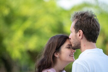 Fototapeta premium Affectionate man kissing woman forehead tender emotional love and trust between couple peaceful romantic gesture in outdoors. Happy couple sharing gentle intimate moment in garden.