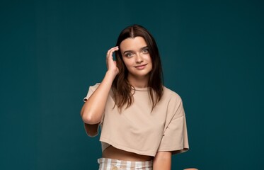 Young woman smiling, hand running through hair, brunette girl showing natural beauty against teal...