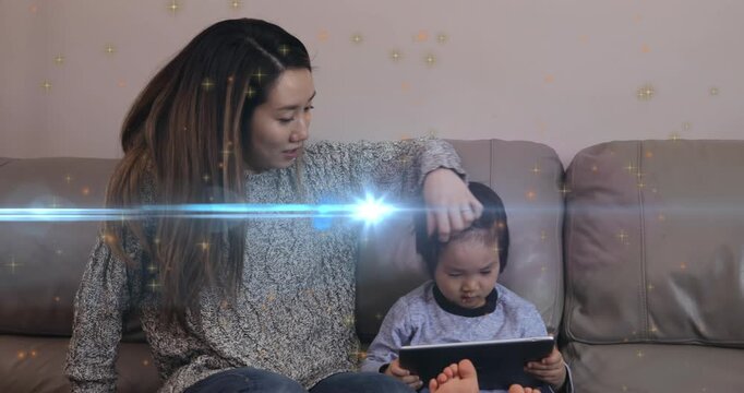 Animation of light moving over happy asian mother and son with tablet sitting on sofa