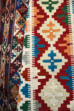 Close-up vertical view of a traditional woven kilim carpet featuring vibrant geometric patterns and symmetrical tribal motifs. Traditional Middle Eastern and Balkan textile art