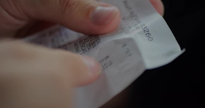 Close-Up of Shopper Hands Holding Long Printed Receipt. Reading Fuel Purchase. Prices, Tax and Total After Payment. Retail Finance. Side View. Accounting and Budgeting Concept. Slow Motion.