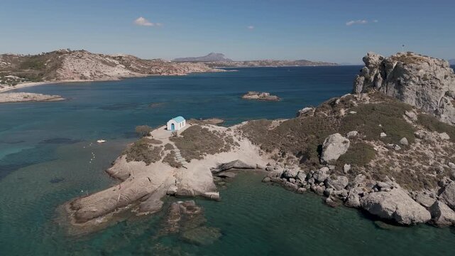 Drone aerial view of white and blue small church in an island in front of Agios Stefanos Beach in Kos Greece