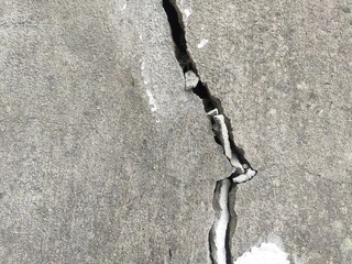 A dangerous deep concrete crack splitting a gray solid foundation. For structural integrity reports, earthquake damage concepts, and repair guides.