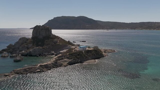 Drone aerial view of white and blue small church in an island in front of Agios Stefanos Beach in Kos Greece
