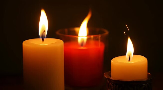Three lit candles of different colors and sizes with flames glowing