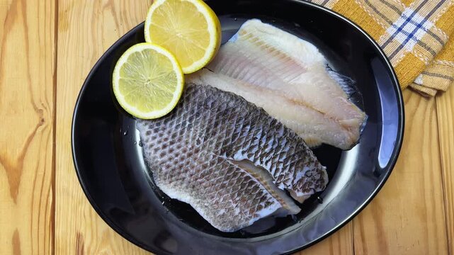Raw defrosted dourade fillets on black plate on rustic table
