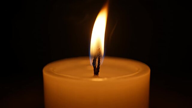 Close up of a lit candle flame glowing in a dark room