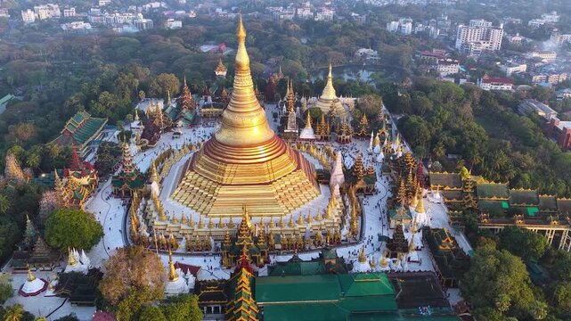 Aerial drone view at Shwedagon Pagoda, a golden stupa, surrounded by lush greenery and urban development in Yangon (Rangun), Myanmar (Burma), showcasing the city's blend of religious and modern life.