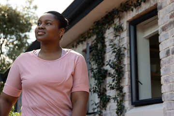 African American woman standing, looking up by ivy brick wall, open window, pink top, hoop earrings © wavebreak3