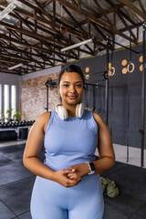 Asian woman standing centered in gym wearing light blue athletic outfit with headset and smartwatch