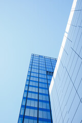 Modern skyscraper building exterior facade under clear blue sky low angle view. Minimalistic repetitive windows made of reflective glass. Financial district buildings, contemporary architecture.