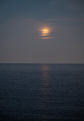 Obraz premium The moon casts its gentle glow on the calm waters, revealing a mesmerizing reflection that elicits feelings of wonder and serenity beneath a serene night sky.