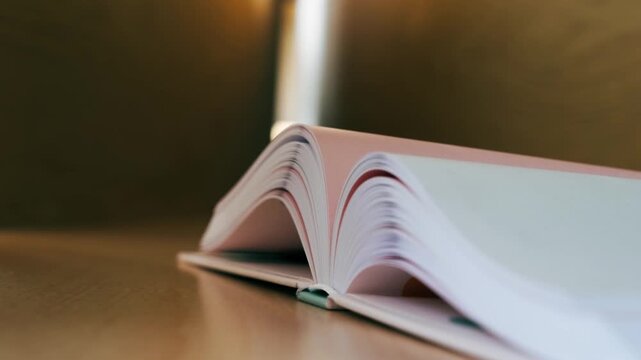 Open hardcover book lying on a desk with flexible pages rising and gently waving, symbolizing the growth of knowledge and learning.