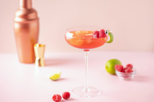 Raspberry daiquiri cocktail with berries and lime zest in an elegant glass on a pink background
