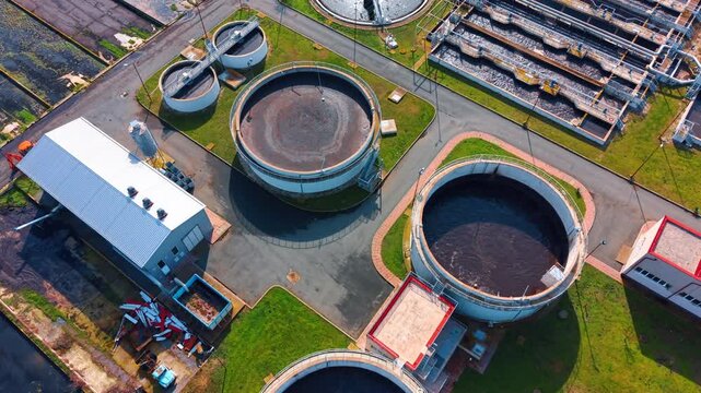 Water treatment facility seen from above. The view shows a water treatment facility with large circular tanks and buildings next to them during daytime.