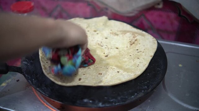Woman pressing and rotating traditional flatbread paratha on a tawa with a cloth
