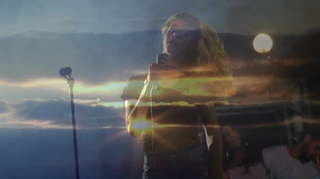 Music cueing female singer lifting mic, singing, standing as sunset bands cross face, performing